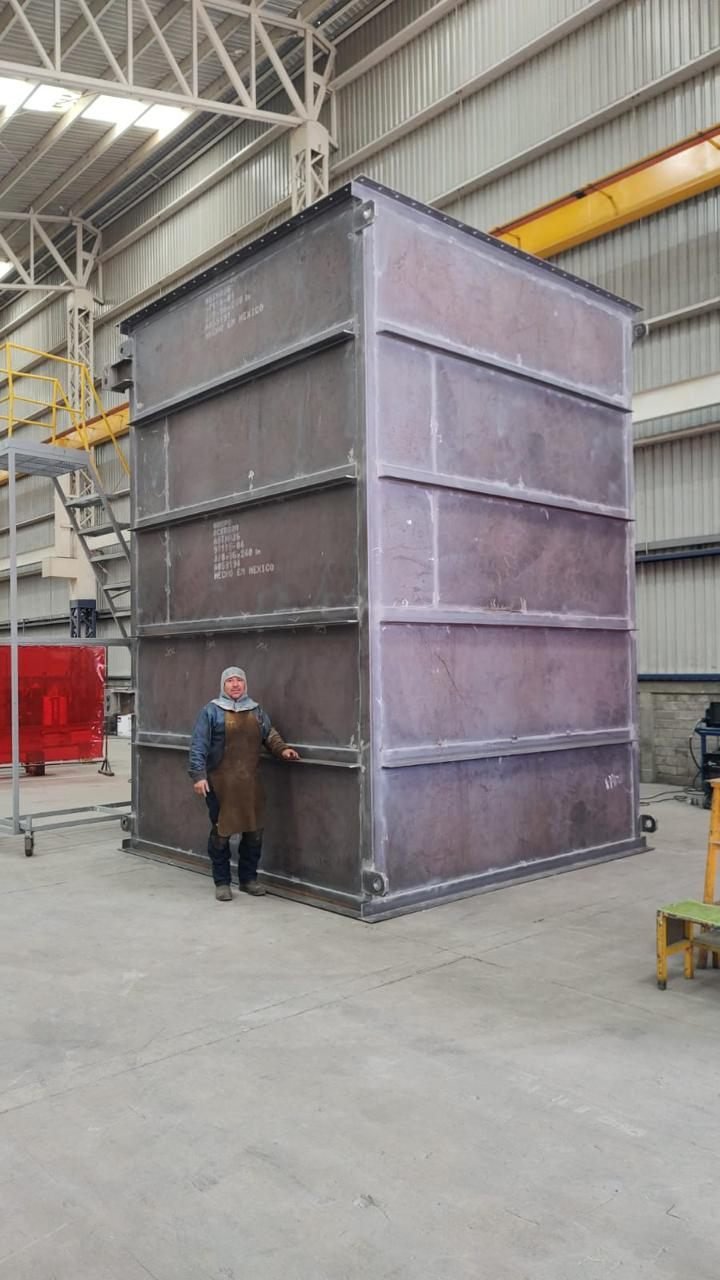 Fabricator standing beside a full-height transformer tank shell for scale