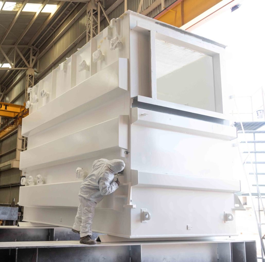 Painter in a full suit inspecting a coated power transformer tank